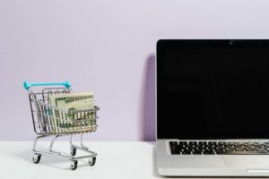 laptop on table with mini cart full of money